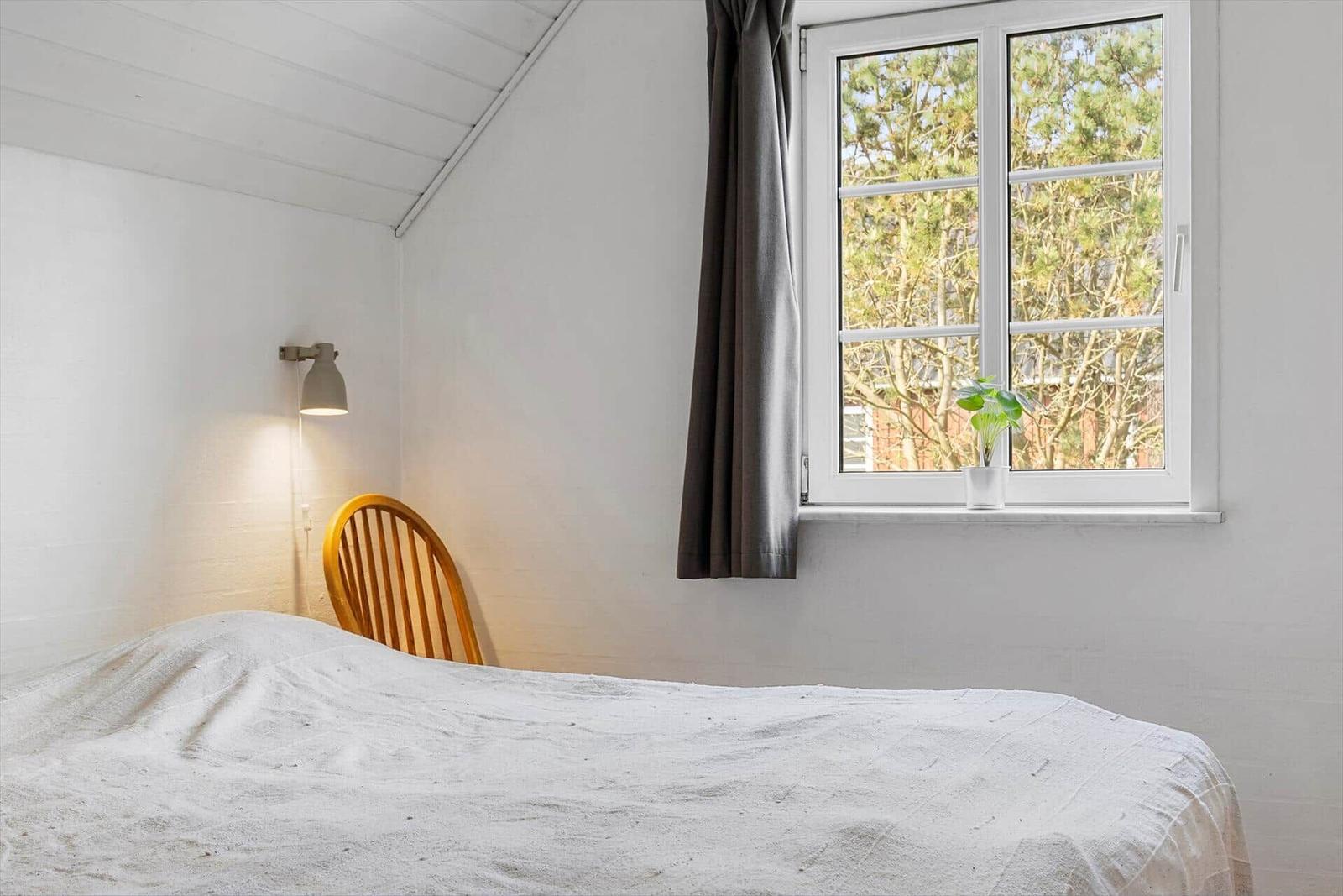 Schlafzimmer mit Bett, Stuhl und Fenster mit Pflanze.