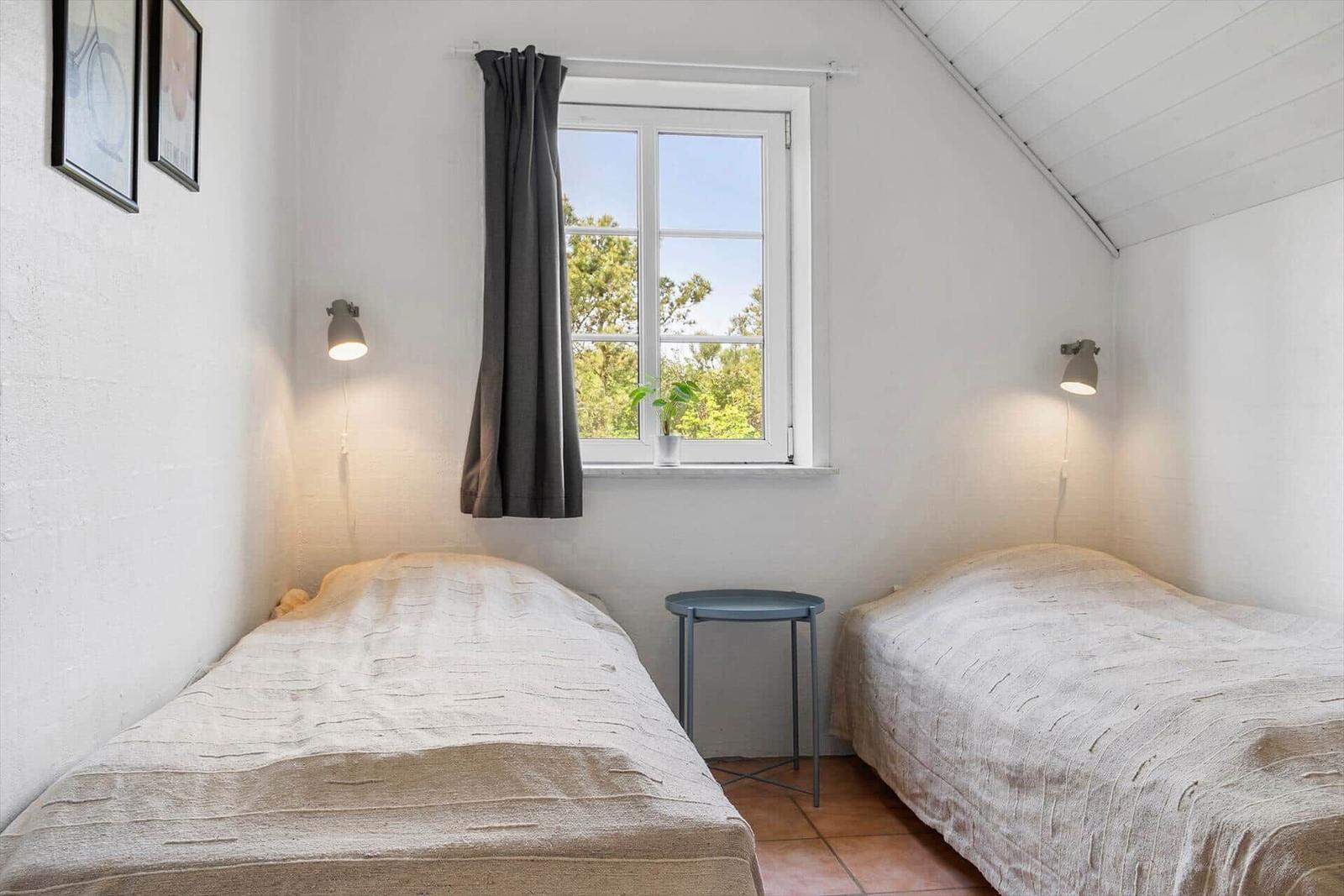 Zwei Betten, ein Fenster mit Blick auf Bäume, Wandlampen und ein kleiner Tisch.