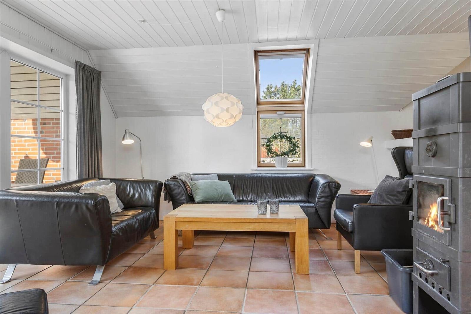 Wohnzimmer mit Leder沙发, Holztisch und Kaminofen. Weiße Wände und Holzdecke.