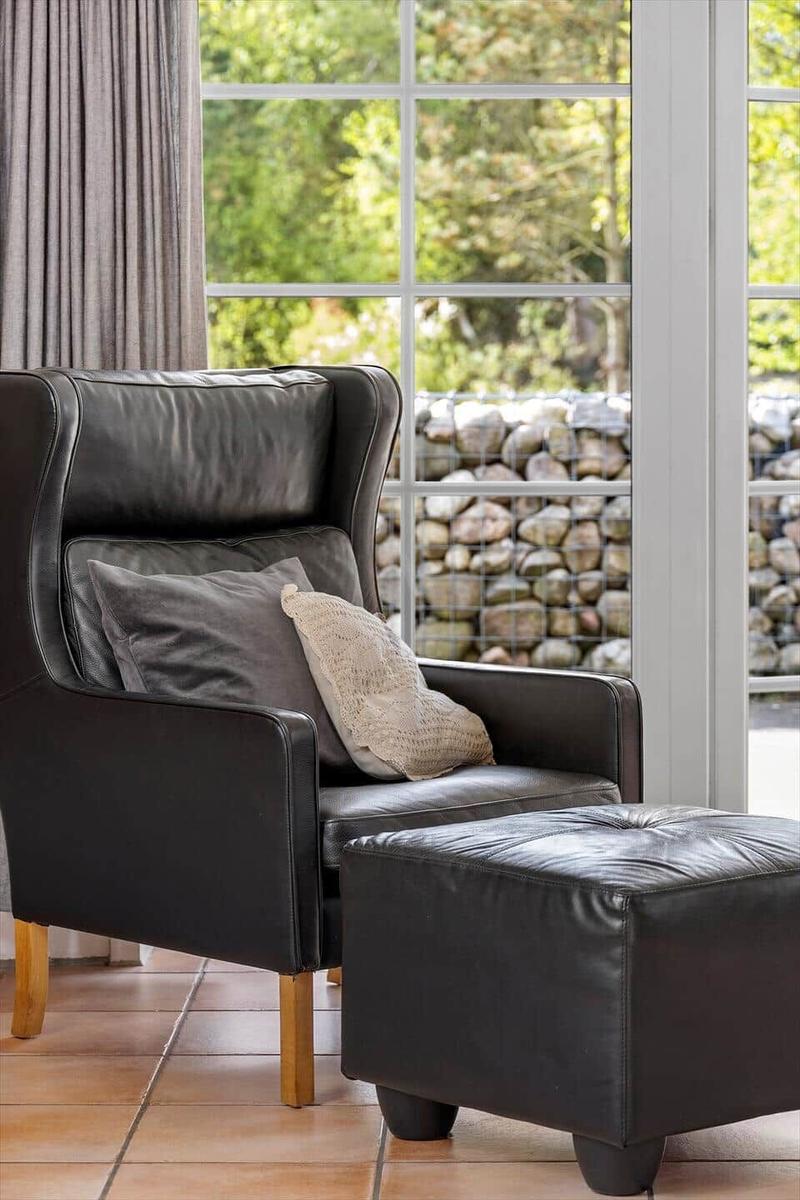 Schwarzer Ledersessel mit Kissen und Fußhocker vor großem Fenster mit Steinmauerblick.