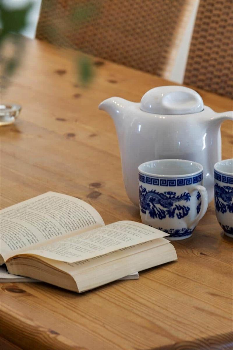 Holztisch mit Teekanne, Tassen und offenem Buch.