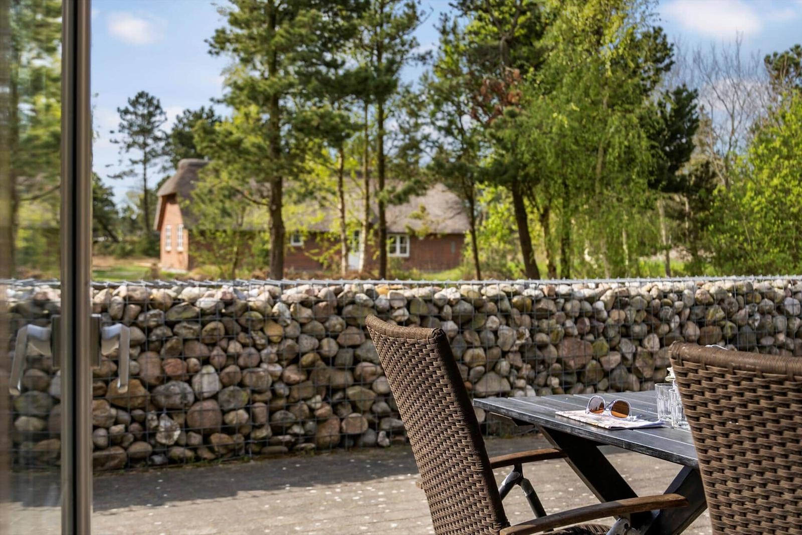 Terrasse mit Tisch und Stühlen. Steinmauer und Wald im Hintergrund.