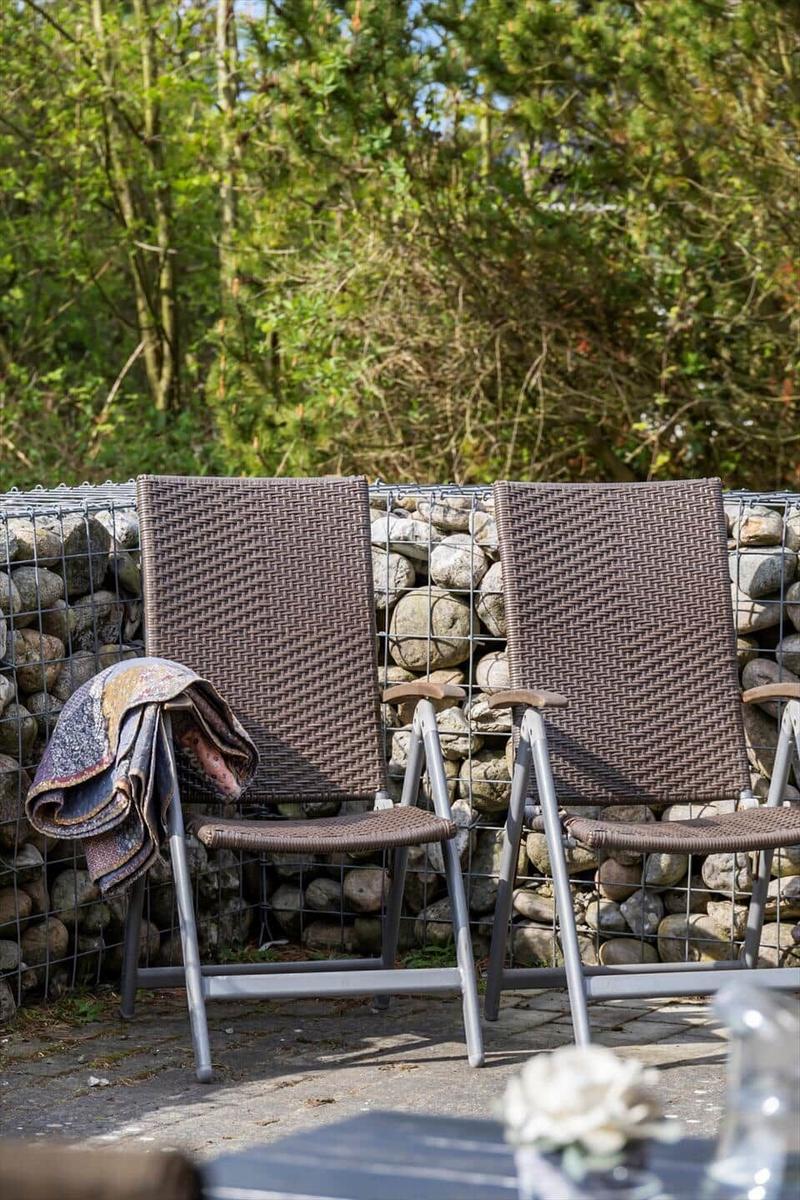 Zwei Stühle mit Decke stehen vor Steinmauer und Bäumen.