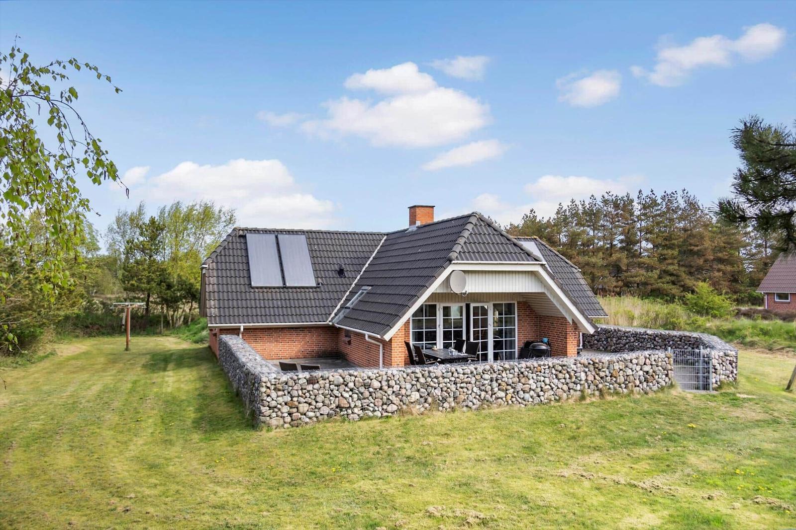 Ein Haus mit Steinmauer, Terrasse und Solaranlage im Grünen.