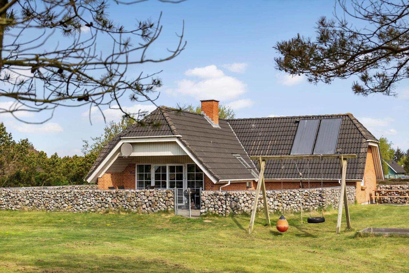 Ein Haus mit Steinmauer, Schaukel und Solaranlage auf dem Dach.