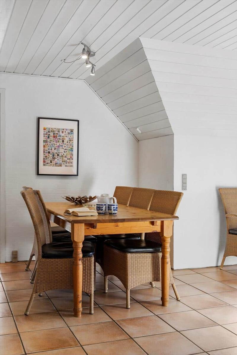 Essbereich mit Holztisch, Rattanstühlen und Wandbild unter schrägem Dach