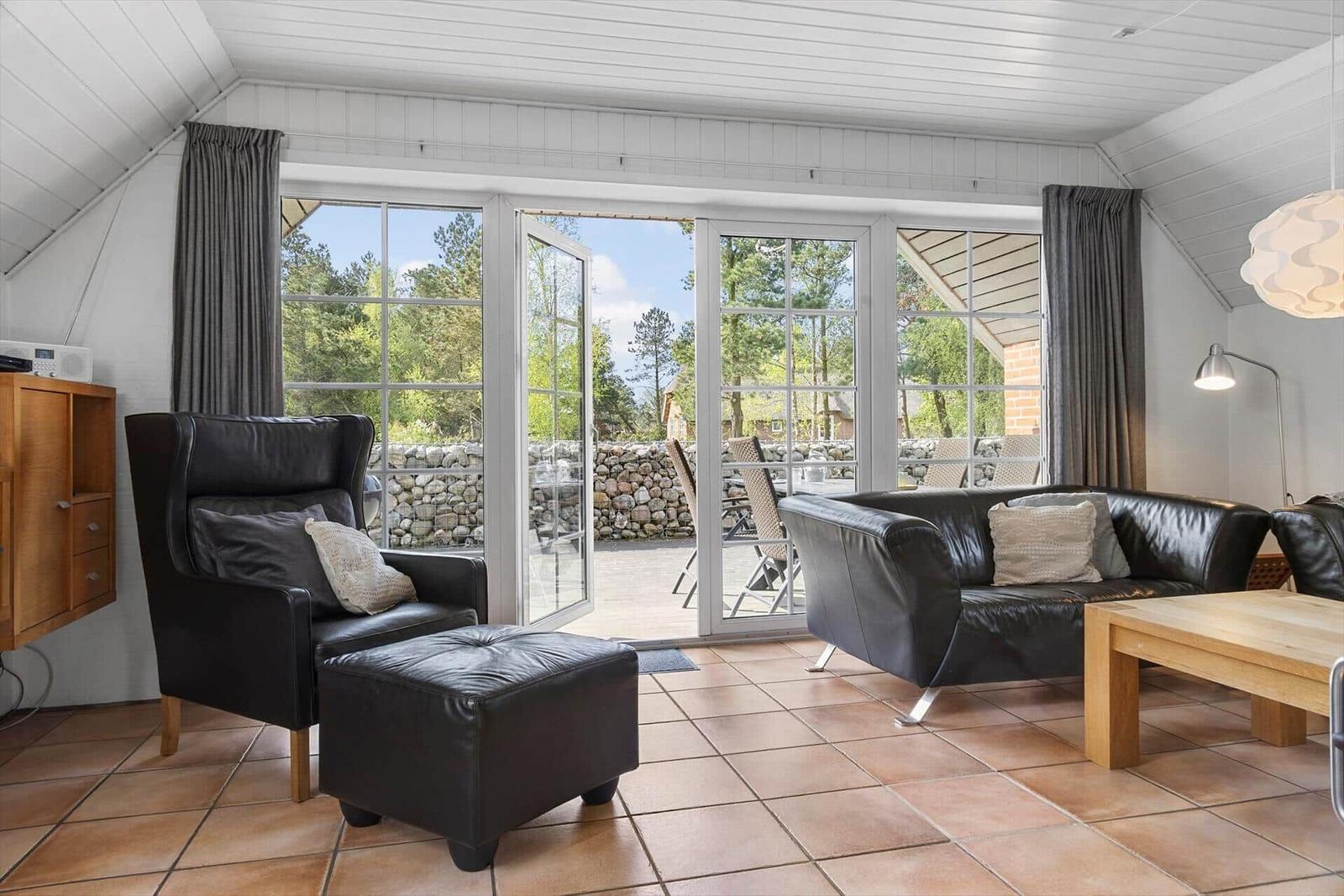 Wohnzimmer mit Ledersofa, Sessel und Terrasse mit Blick auf Wald.