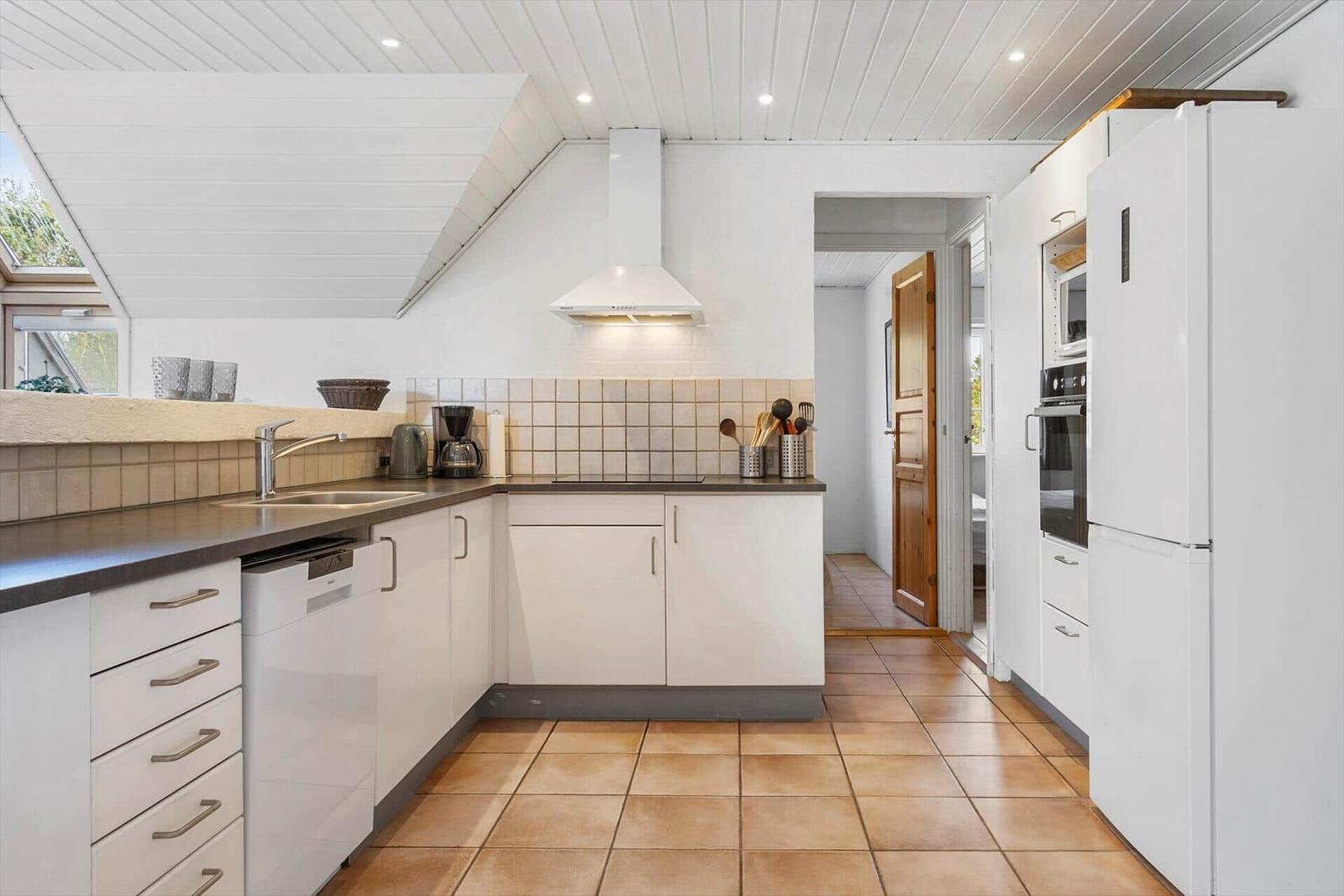 Küche mit weißen Schränken, dunkler Arbeitsplatte und Terrakottafußboden.