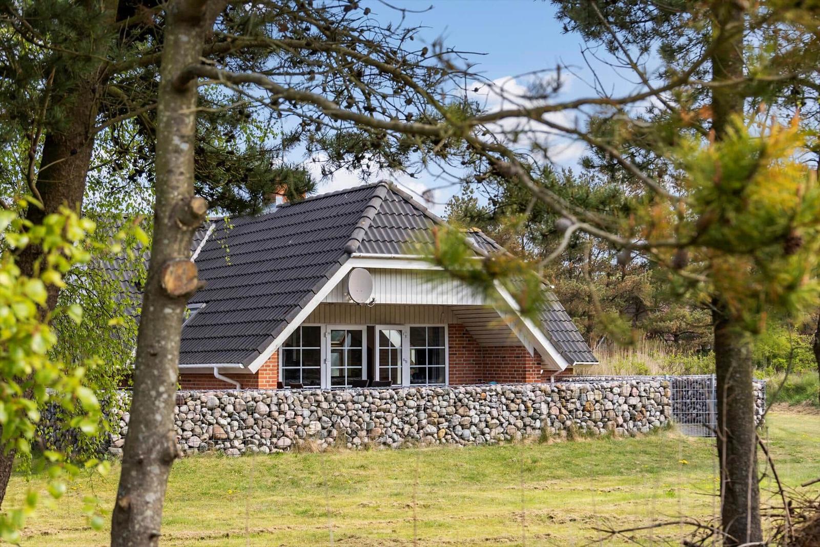Haus mit Steinmauer und großen Fenstern, umgeben von Bäumen.