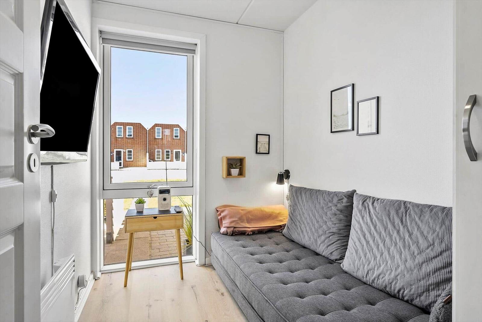 Ein Raum mit grasem Sofa, Fernseher und Fensterblick auf Häuser.