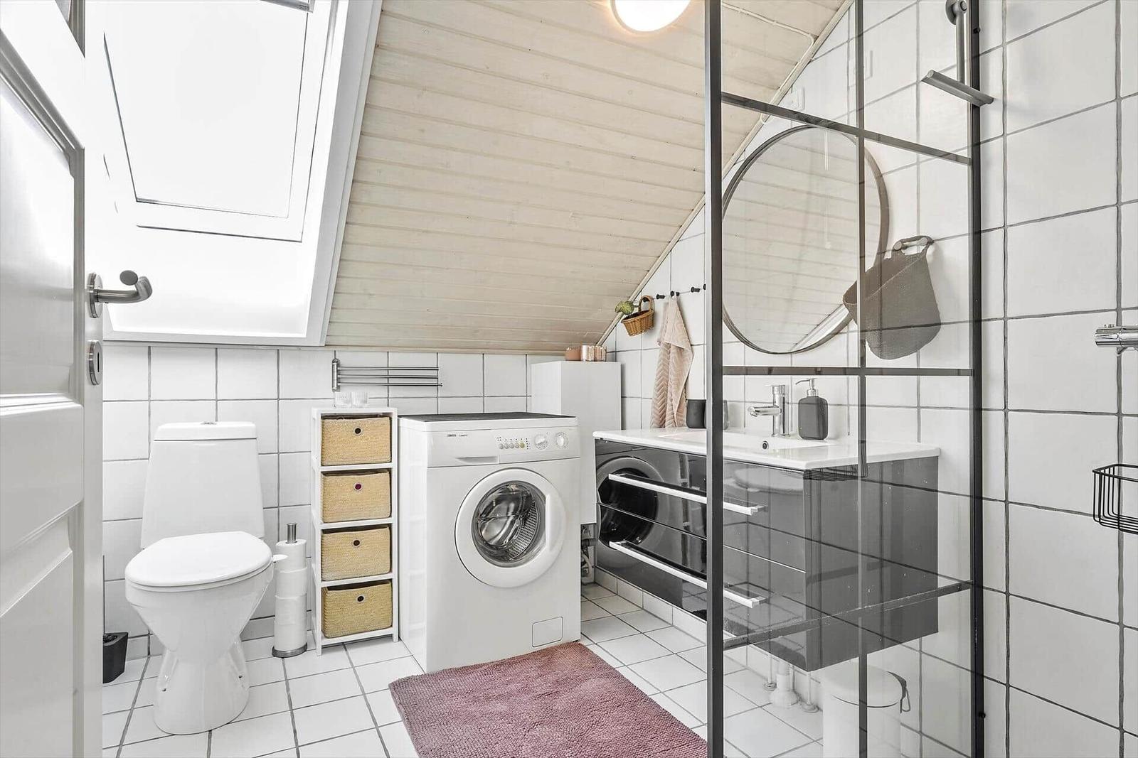 Badezimmer mit Dusche, Waschmaschine und Toilette unter Dachschrägen.