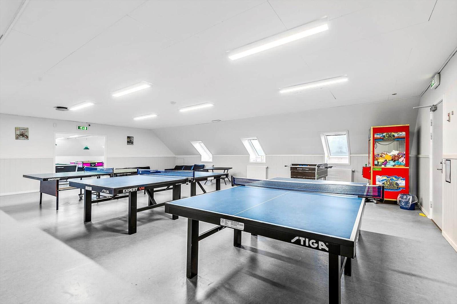Raum mit mehreren Tischtennisplatten und einer Spielmaschine.