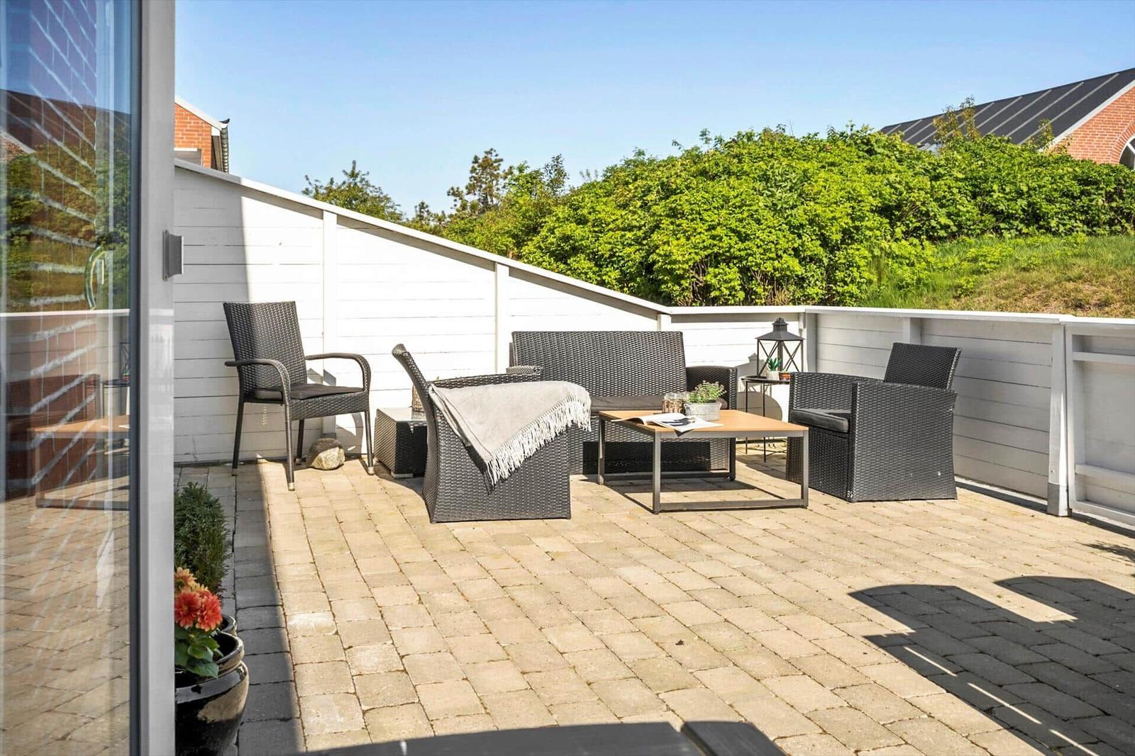 Terrasse mit Sitzgruppe und Tisch, umgeben von weißen Wänden und Grün.