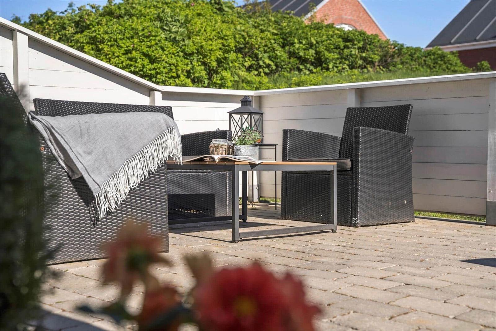 Terrasse mit Gartenmöbeln, Tisch und Decke. Hintergrund: grüne Hecke und Hauswand.