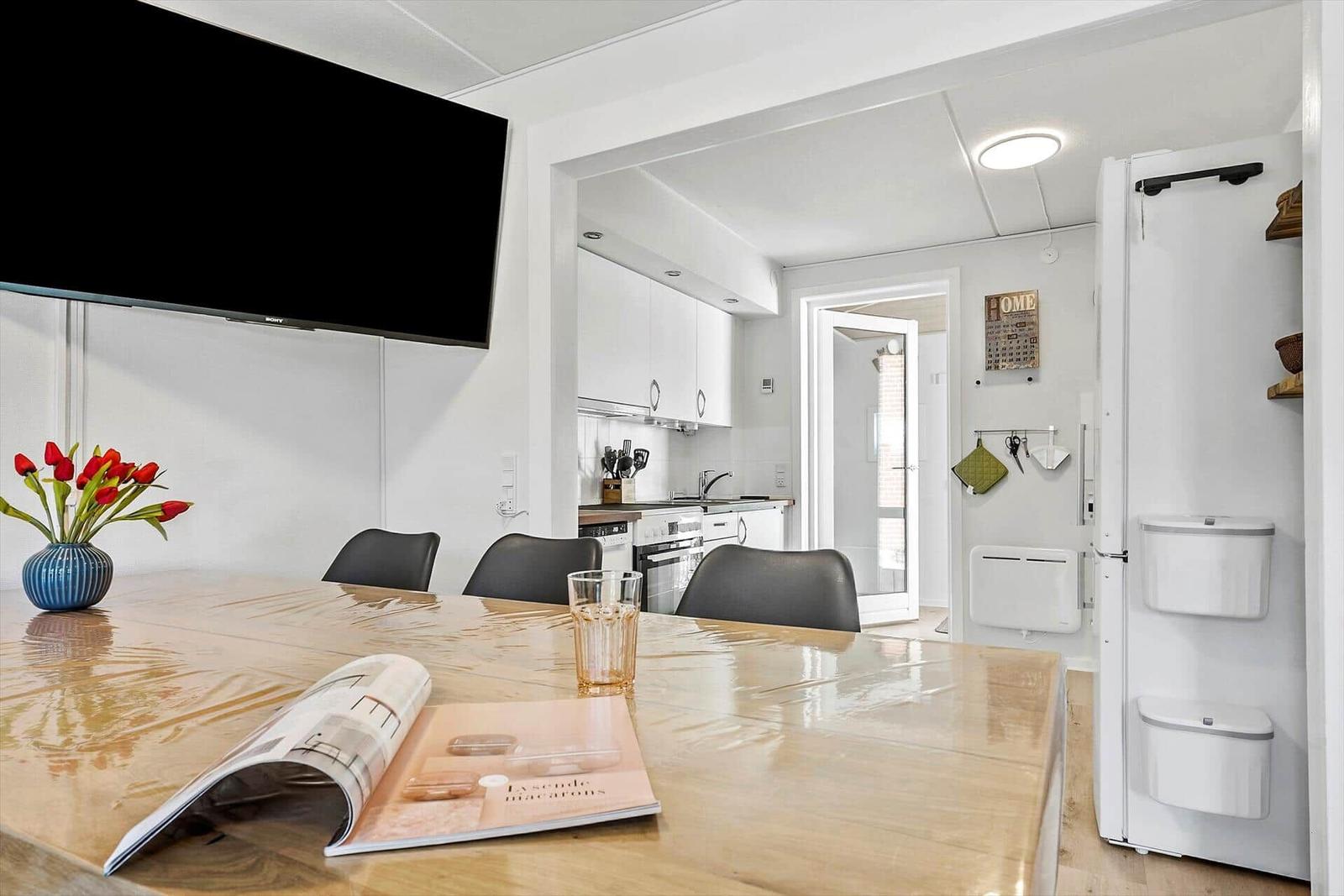 Essbereich mit Holztisch, Fernseher und Blick in die Küche.