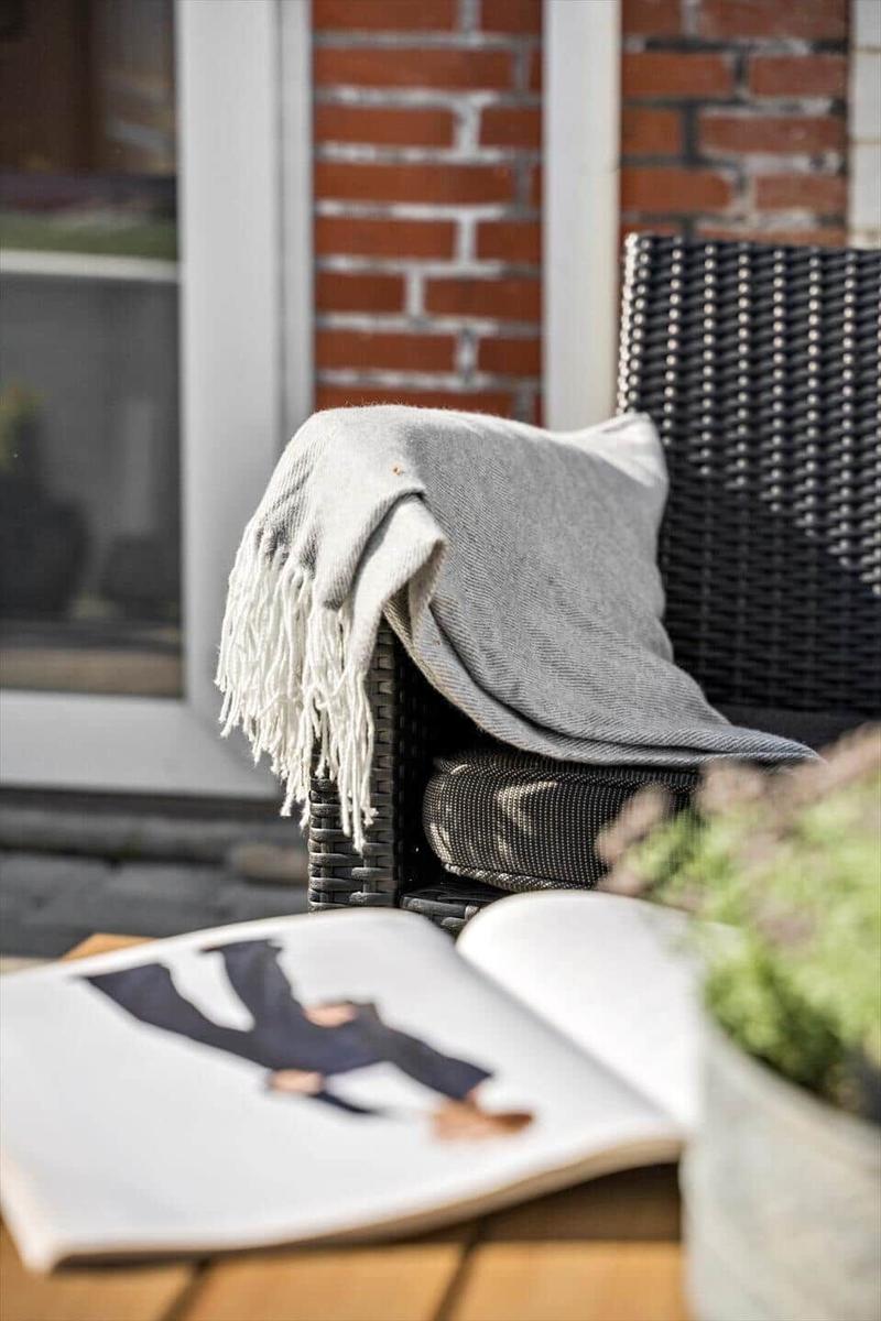 Schwarzer Rattanstuhl mit grauer Decke und offenes Buch auf Tisch.