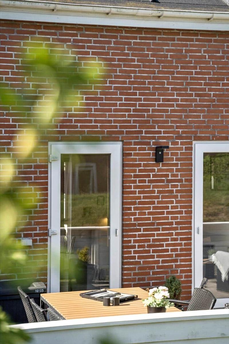 Terrasse mit Tisch und Stühlen vor rotem Backsteinhaus mit Fenstern.
