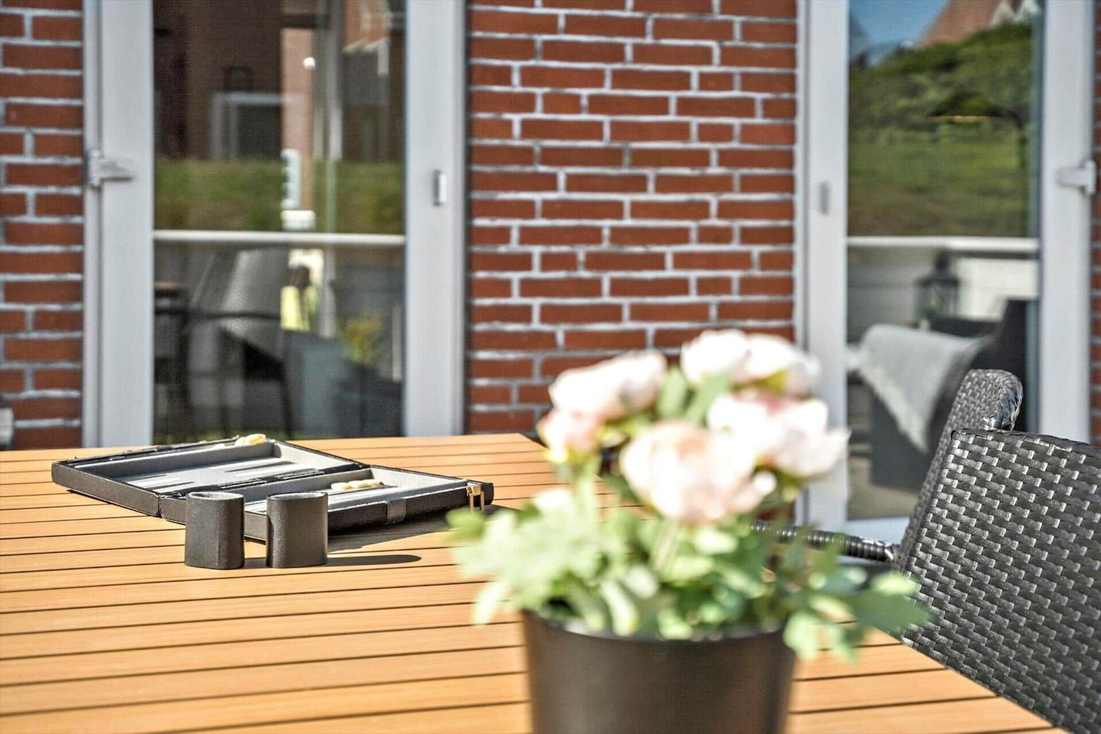 Terrasse mit Holztisch, Stühlen und Blumenarrangement vor Backsteinmauer.