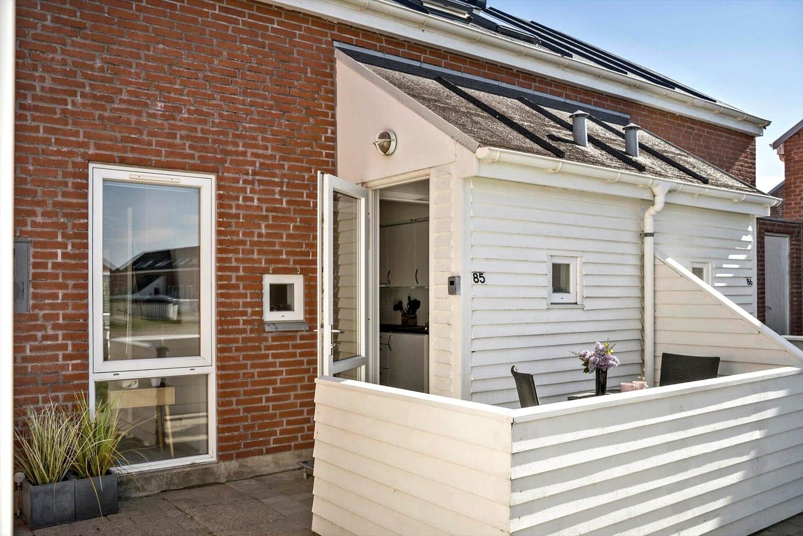 Wohnhaus mit weißen Holzwänden und Terrasse. Tür offen, Blick in Küche.