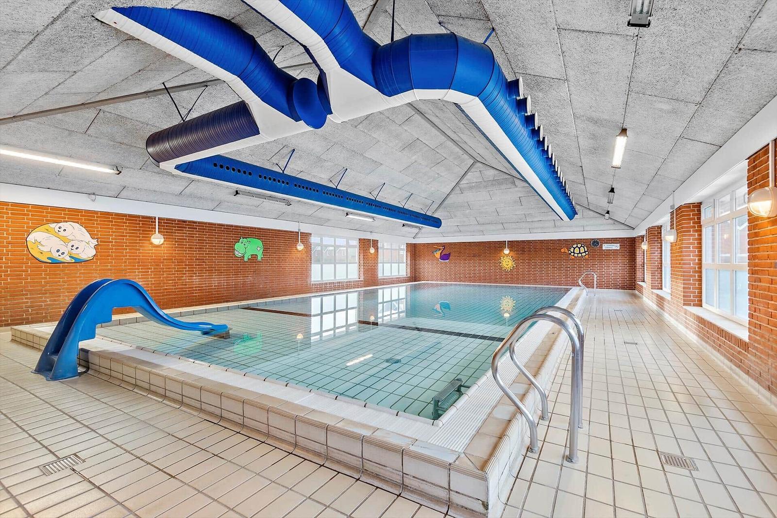 Indoor-Schwimmbad mit blauer Rutsche und kinderfreundlichen Wanddekorationen.