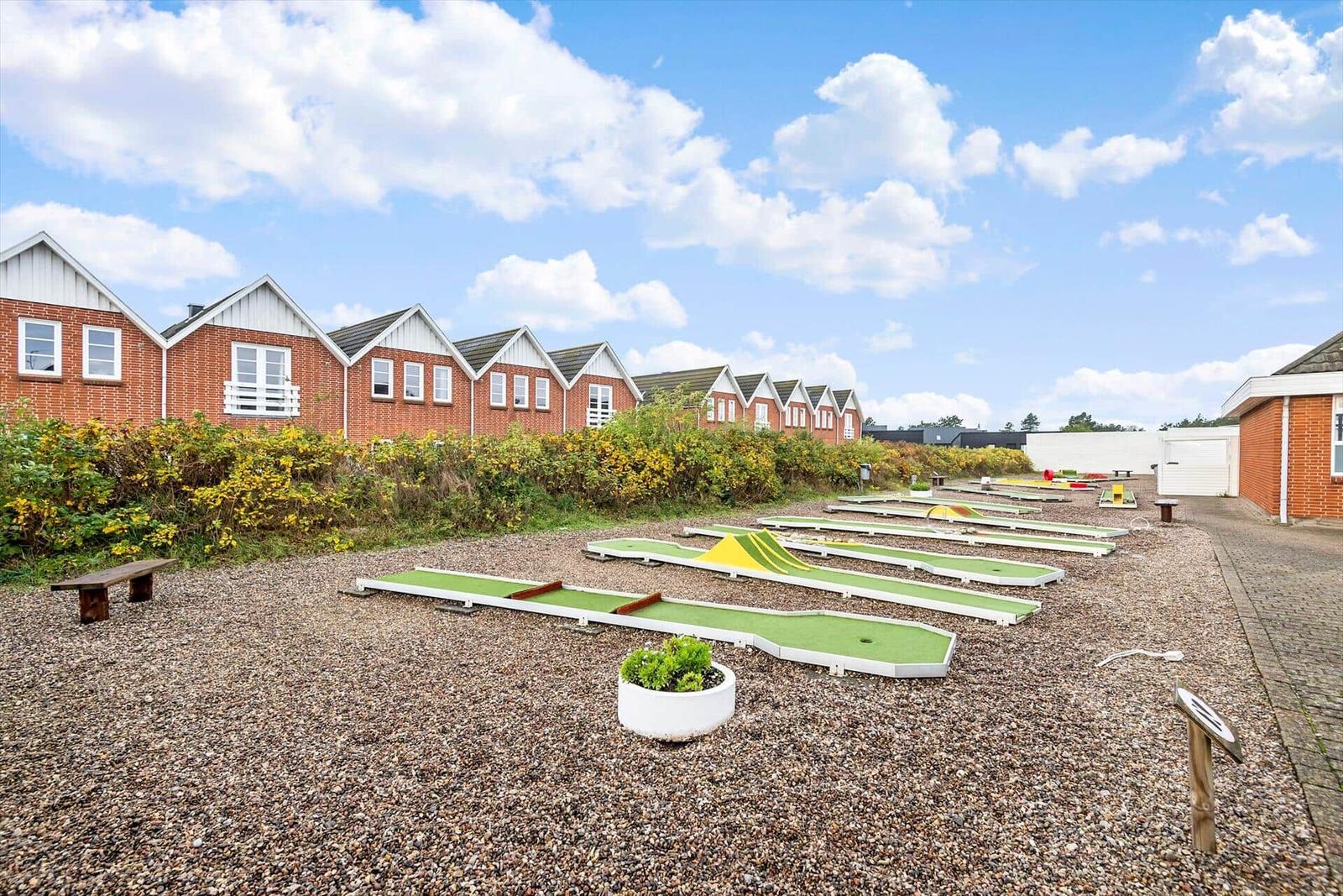 Minigolfplatz mit mehreren Bahnen vor Reihenhäusern auf Kiesgrund.