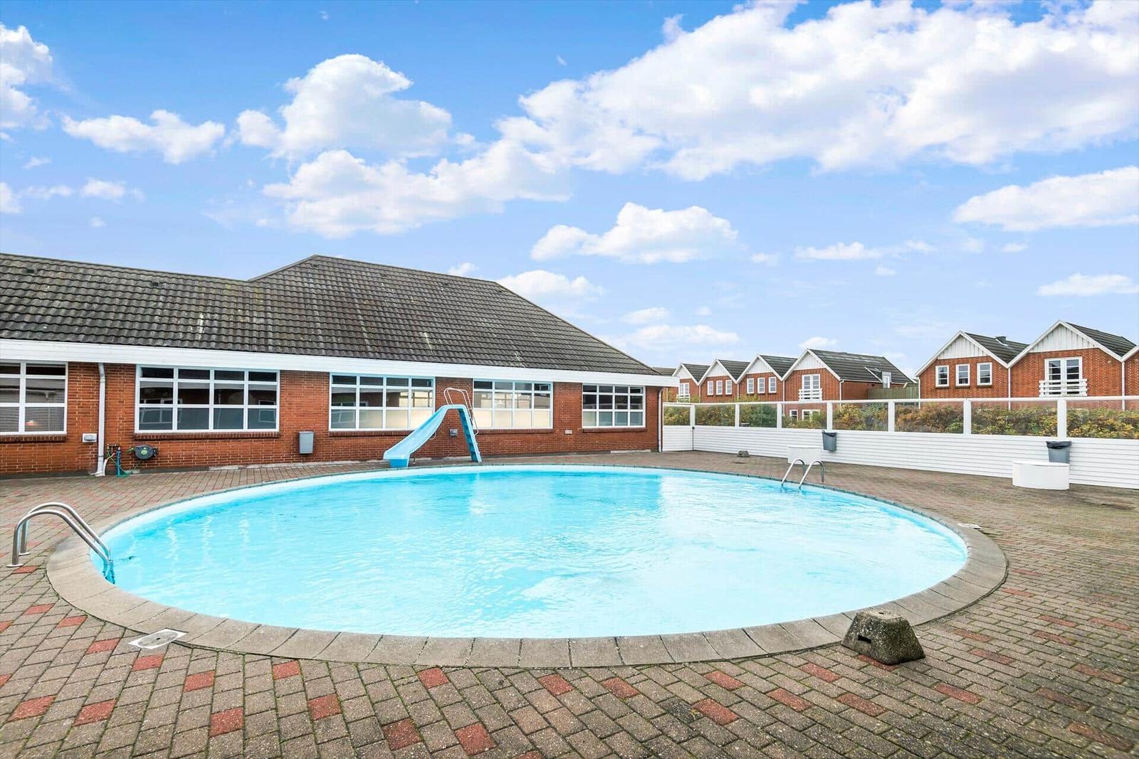Runder Pool mit Rutsche und Terrasse vor einem Gebäude.