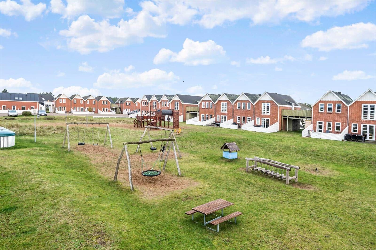Grüner Spielplatz mit Schaukel und Tisch vor Reihenhäusern.