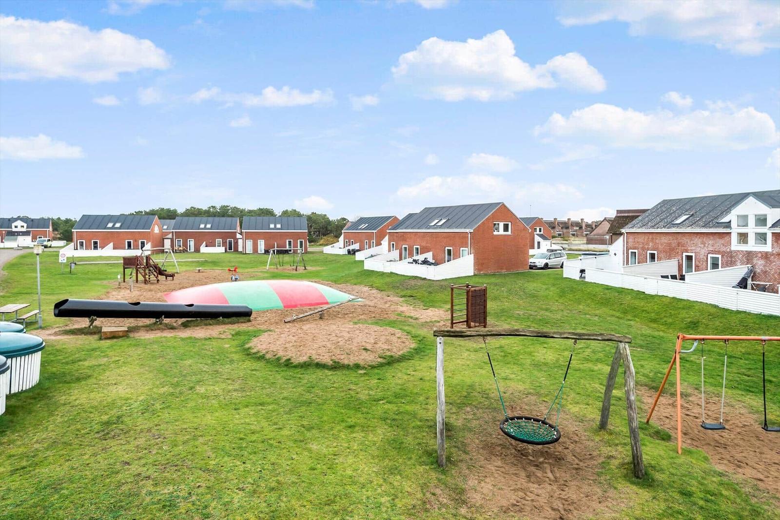 Grüner Spielplatz mit Schaukel und Klettergerüst vor roten Häusern.