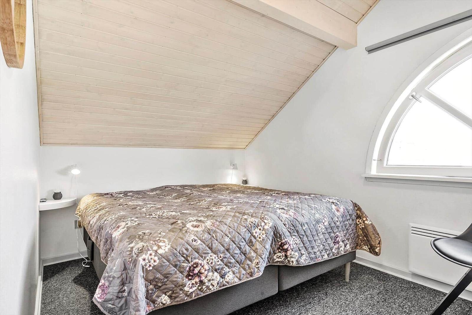Schlafzimmer mit Dachschrägen, Bett mit floraler Decke und Bogenfenster.