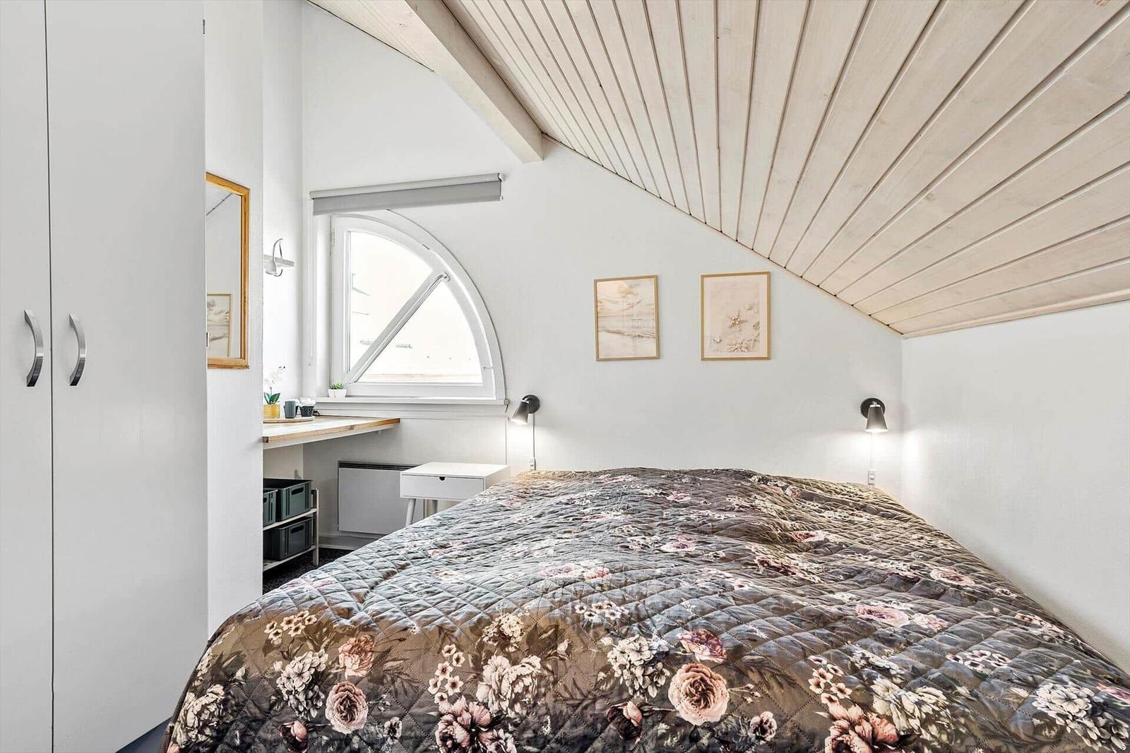 Schlafzimmer mit Dachschrägen, Bett mit Blumenbezug, Fenster und Schrank.