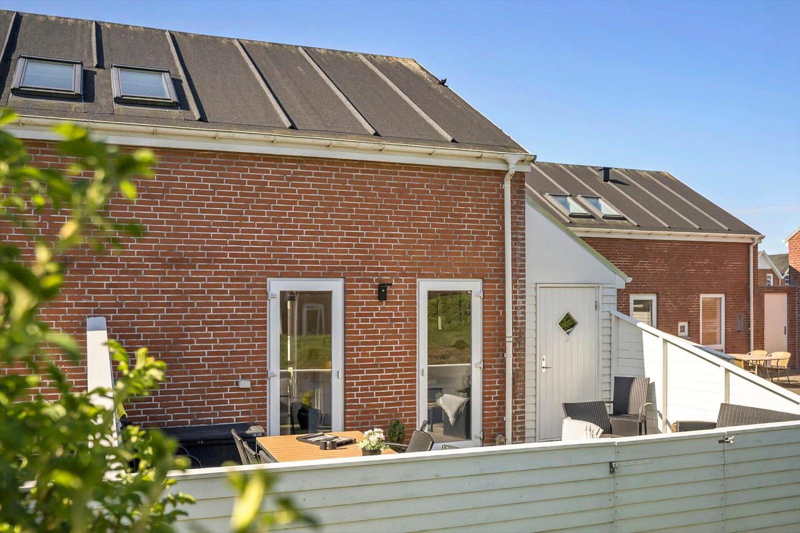 Roter Backsteinbau mit Terrasse und Gartentisch. Weiße Tür und Dachfenster sichtbar.