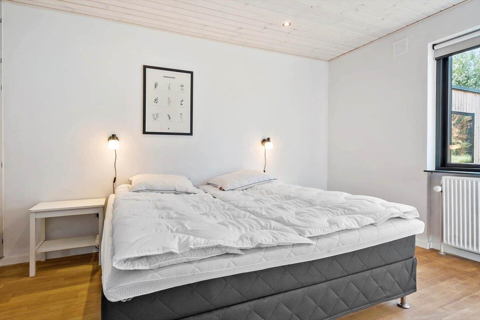Schlafzimmer mit Doppelbett, Nachttisch und Fenster.