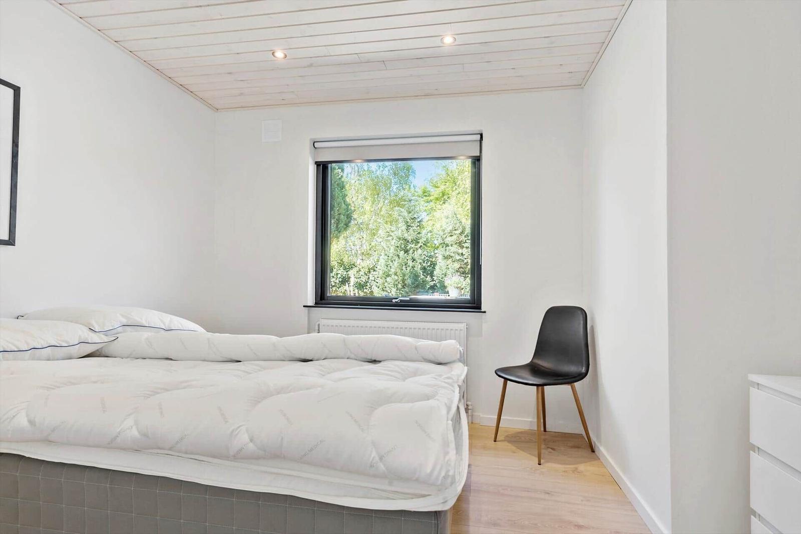 Schlafzimmer mit Bett, Fenster und Stuhl.