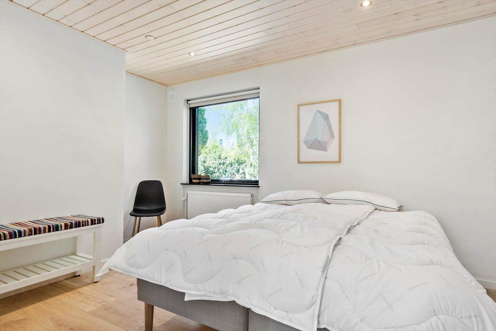 Schlafzimmer mit Bett, Fenster und Holzdecke.