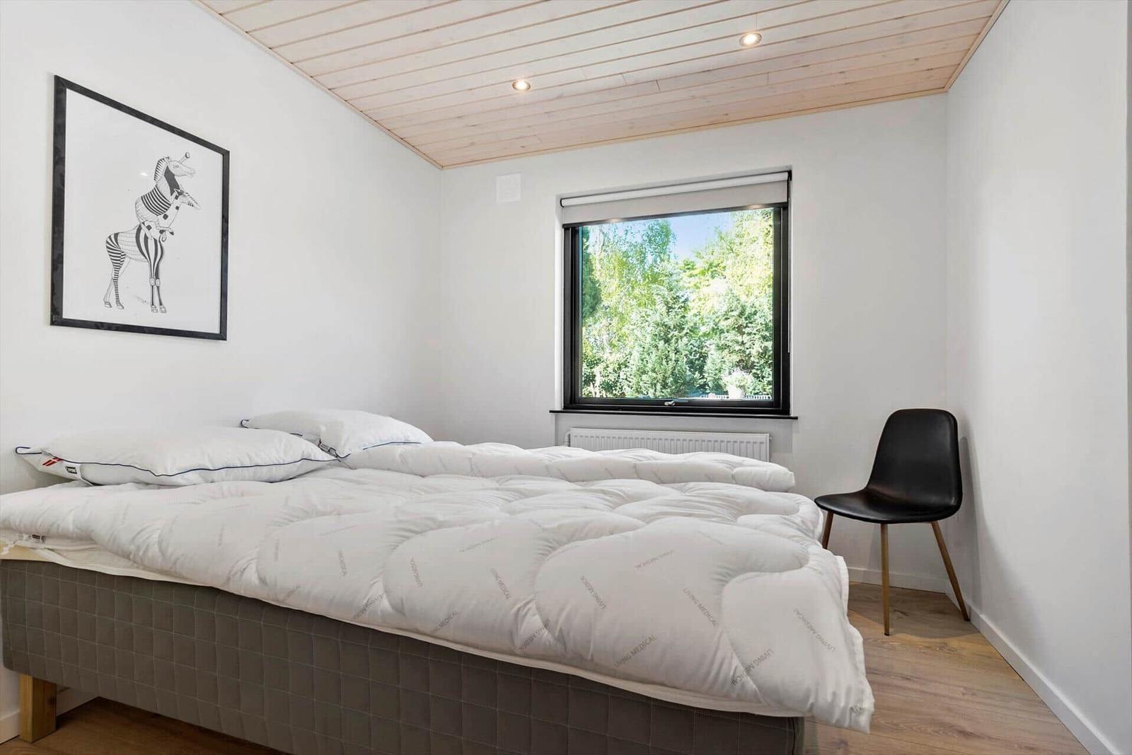 Schlafzimmer mit Bett, Fenster und Stuhl.