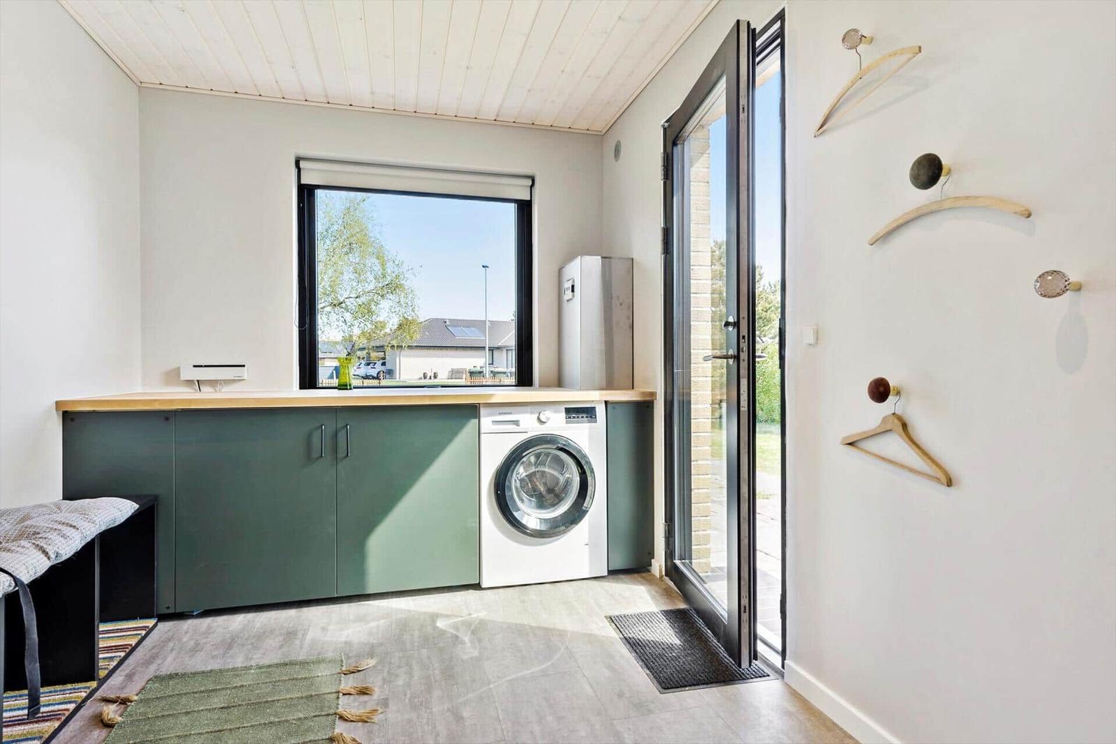 Wohnraum mit Waschmaschine, Fenster und Glastür. Wand mit Haken.