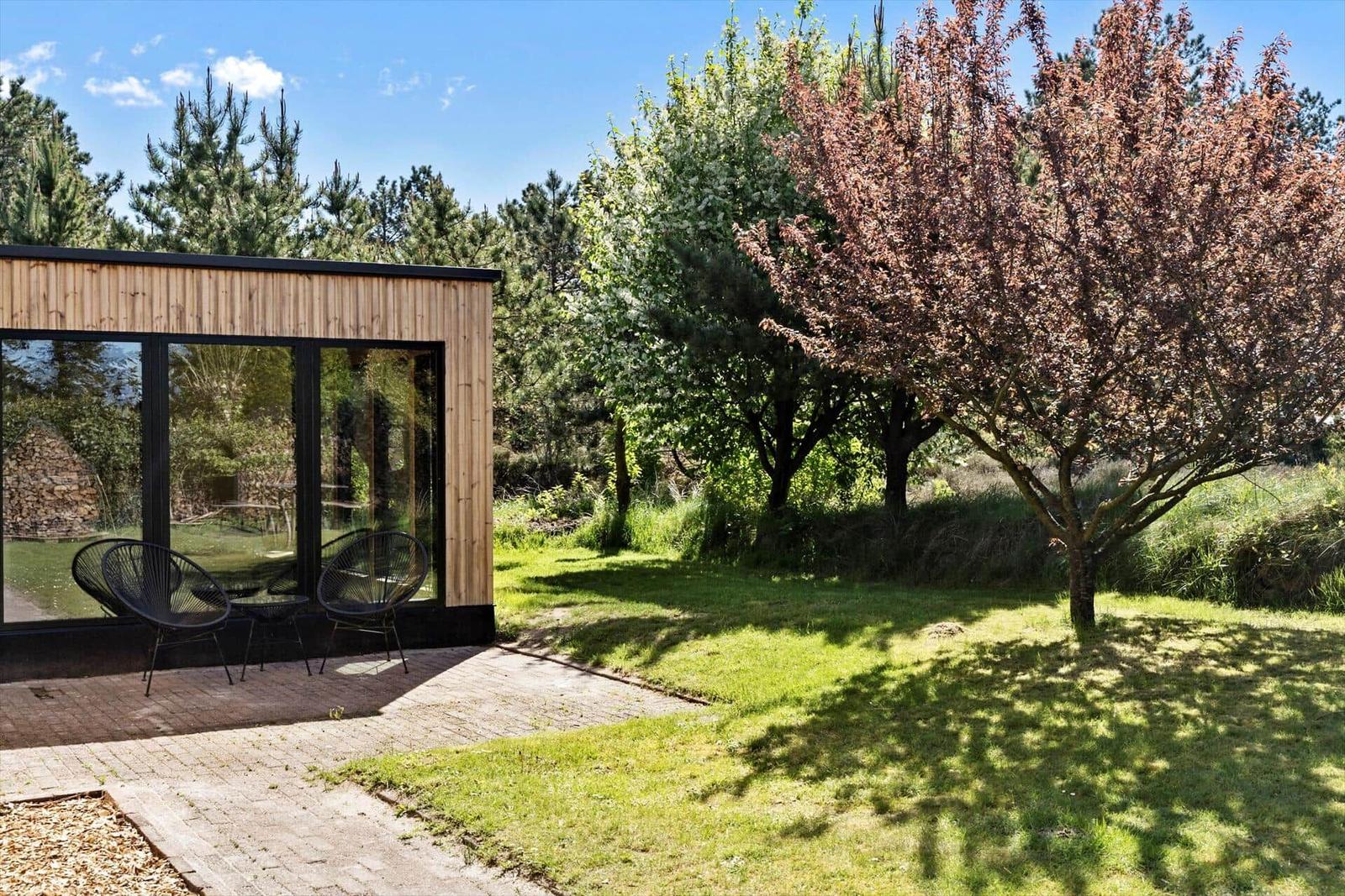 Moderne Hütte mit Glasfront und Gartenbereich unter Bäumen.