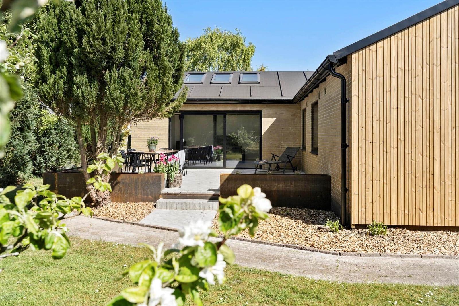 Moderne Villa mit Terrasse, Garten und Holzfassade. Sicht auf Essbereich und Außendeko.