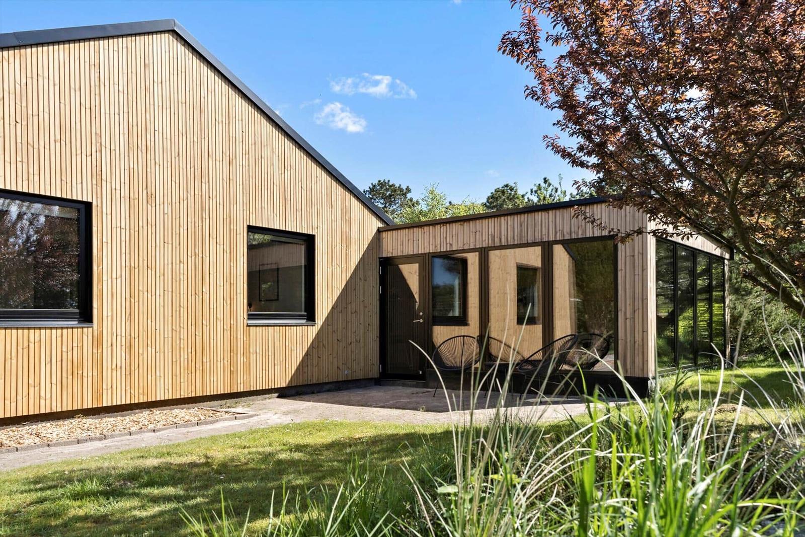 Moderne Holzhütte mit Terrasse und Sitzgelegenheiten im Grünen.