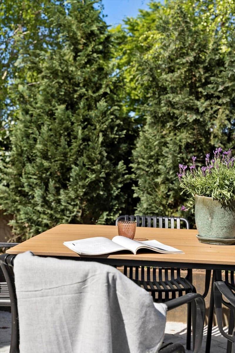 Holztisch mit Stühlen, offenem Buch und Lavendeltopf im Garten.