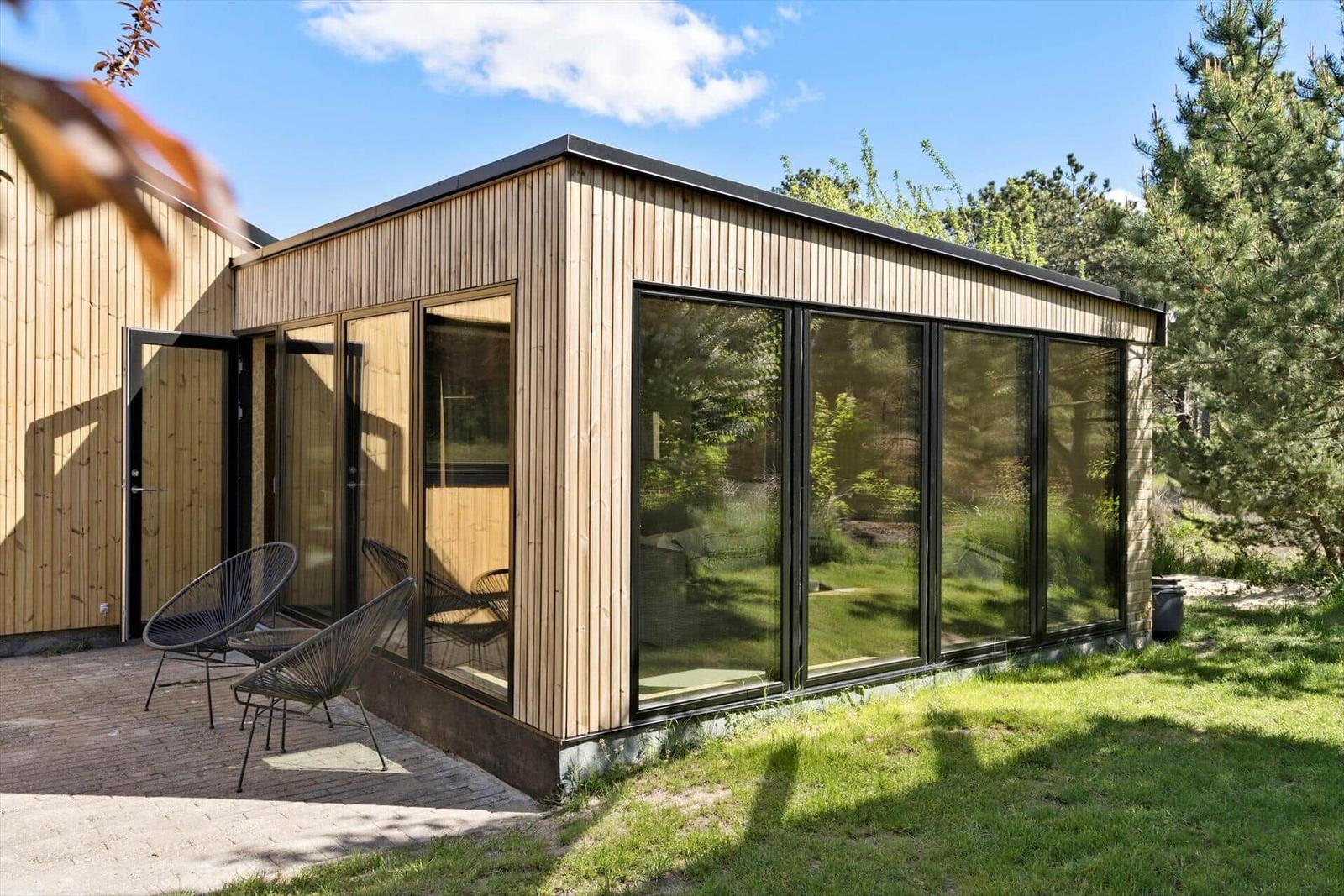 Moderne Holzhütte mit großem Glasbereich und Außenbereich mit Stühlen.