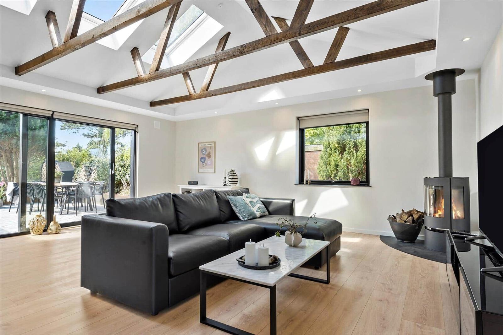 Wohnzimmer mit schwarzer Couch, Kamin und Holzbalken an der Decke.