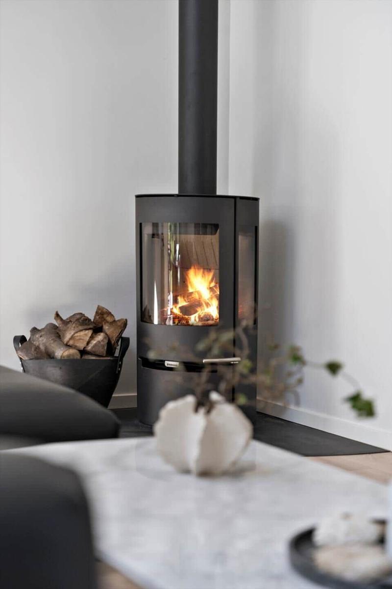 Moderne Feuerstelle mit brennendem Holz und Holzstapel daneben.