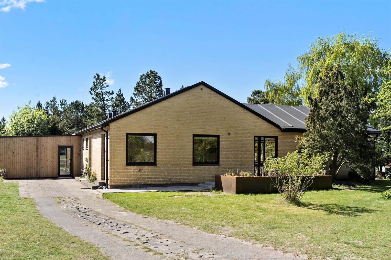 Moderne Villa mit Garten und Holzgarage unter blauem Himmel.