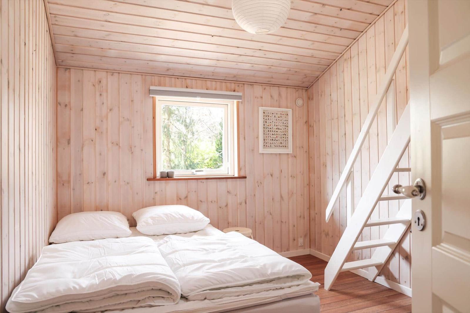 Bedroom with wooden walls, window and white mattress.