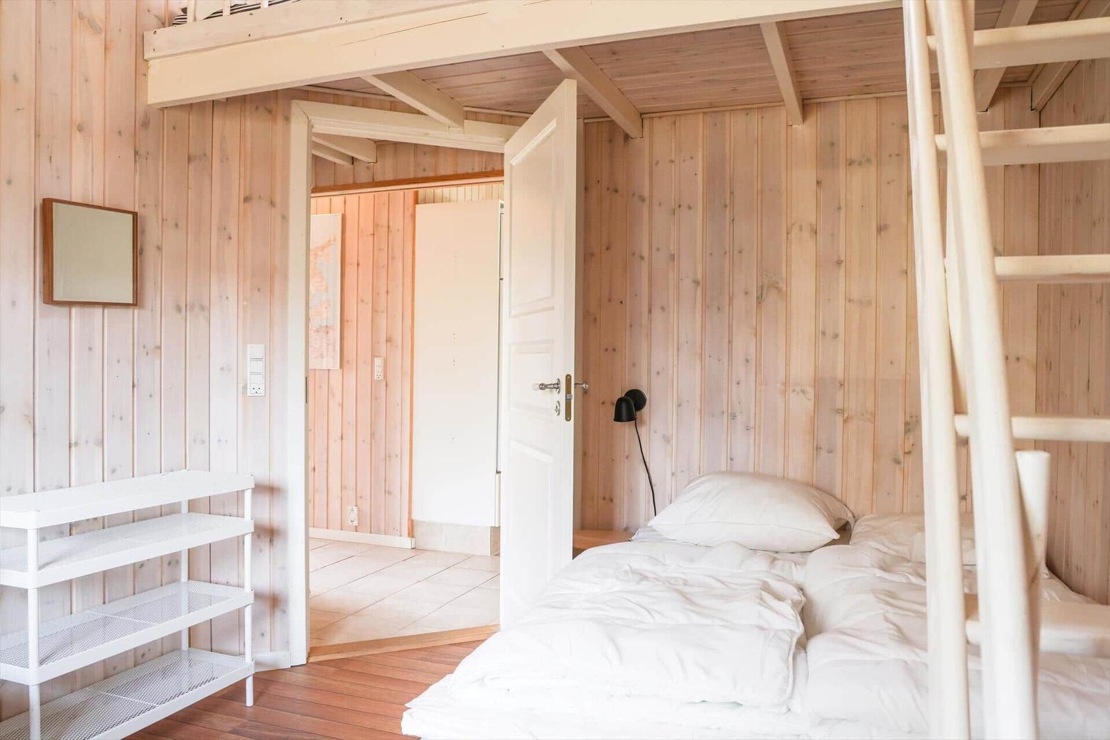 Bedroom with double bed and wooden walls. Ladder leads to upper level.