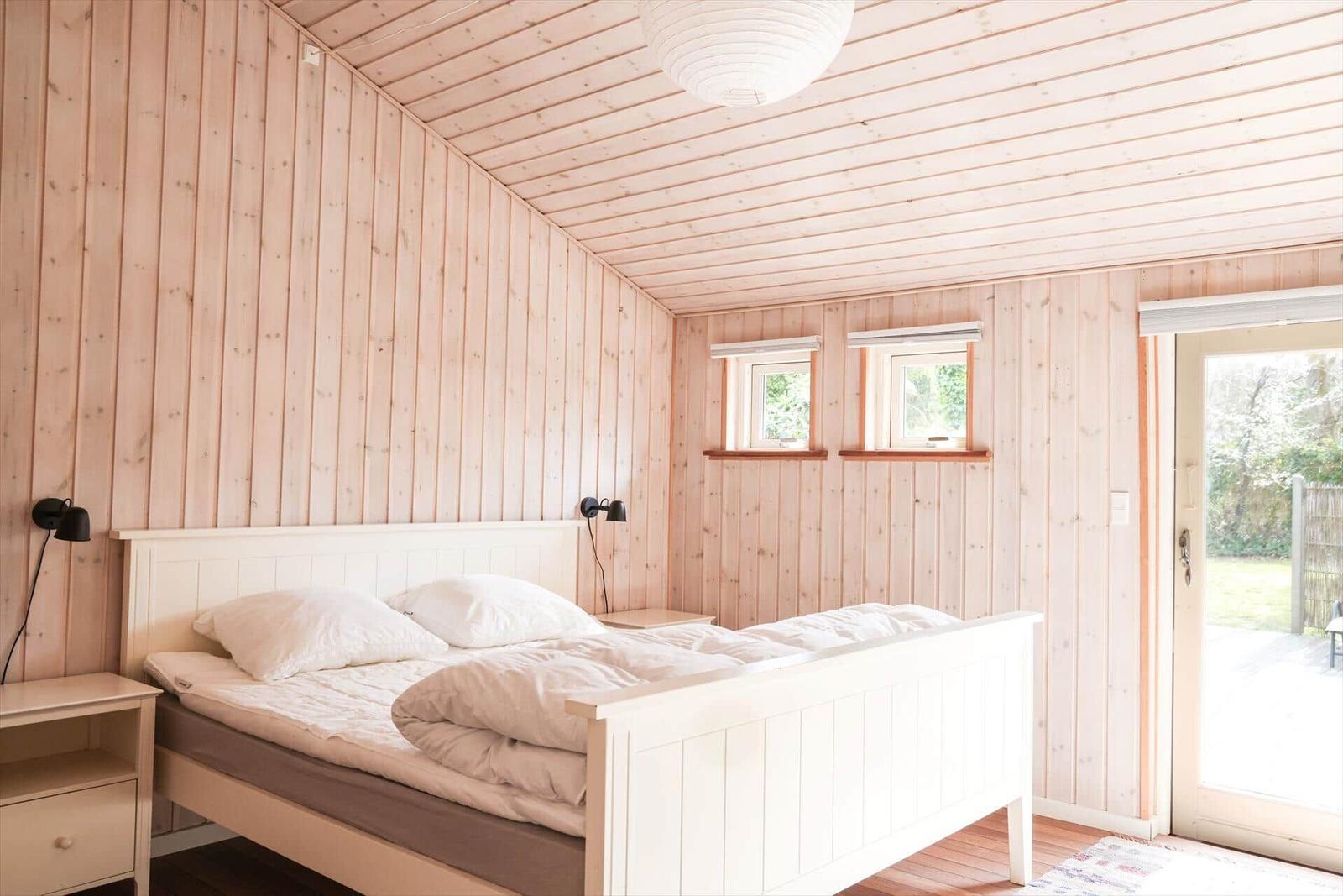 Bedroom with wooden walls, bed, and door to the garden.
