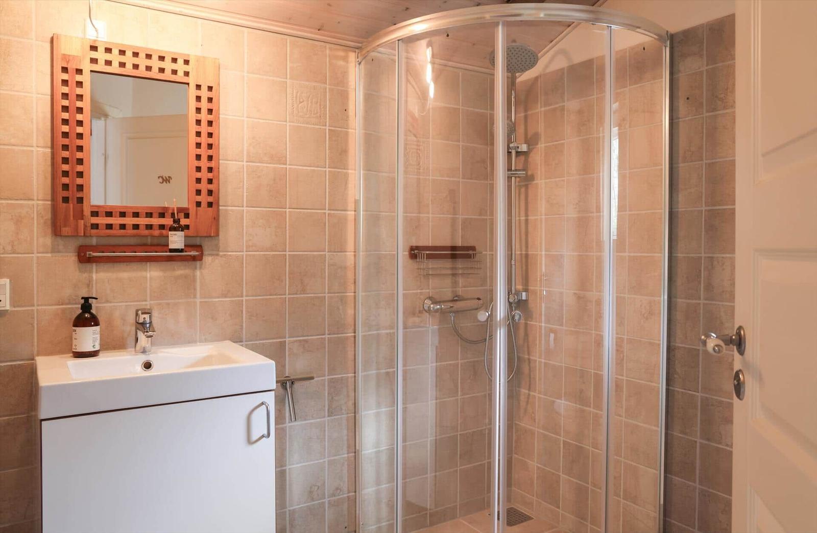 Bathroom with shower and sink. Wood mirror and tiled wall.
