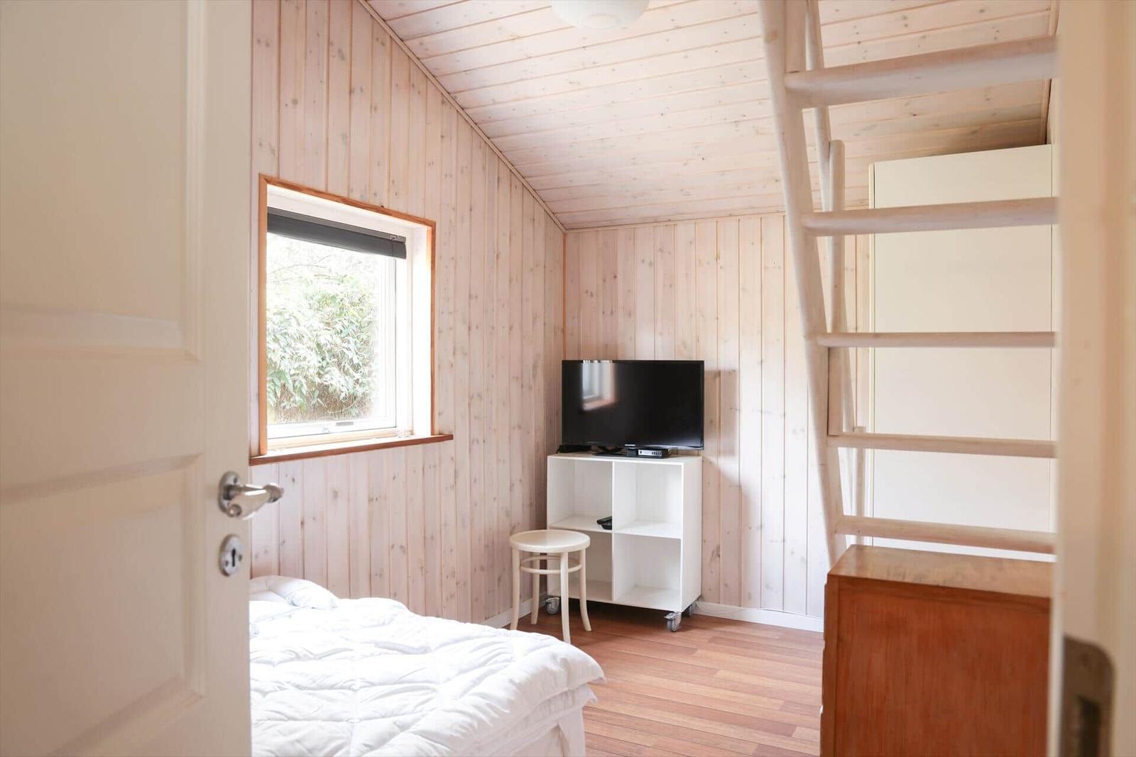 Bedroom with bed, TV, and window. Wooden walls and floor.