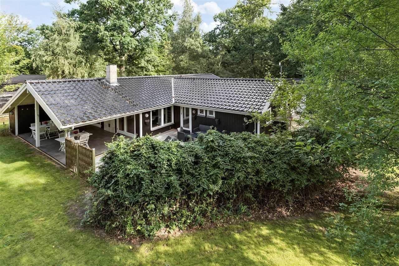 Wooden house with terrace, garden, and surrounding trees.